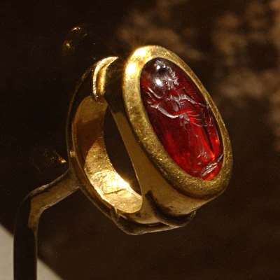 A massive gold signet ring with a red engraved stone set across the hand.