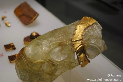 A photo taken at the museum shows the vessel lying on display. A beaker is narrow with a conical body, slightly expanding upwards, it is decorated with large round concave medallions. The glass is colorless, slightly translucent. In an arc from the upper edge through the center of the vessel, there is a band made of gold covering the crack.